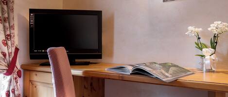 Une pièce avec un bureau en bois, une télévision, une chaise, un livre et un vase rempli de fleurs.