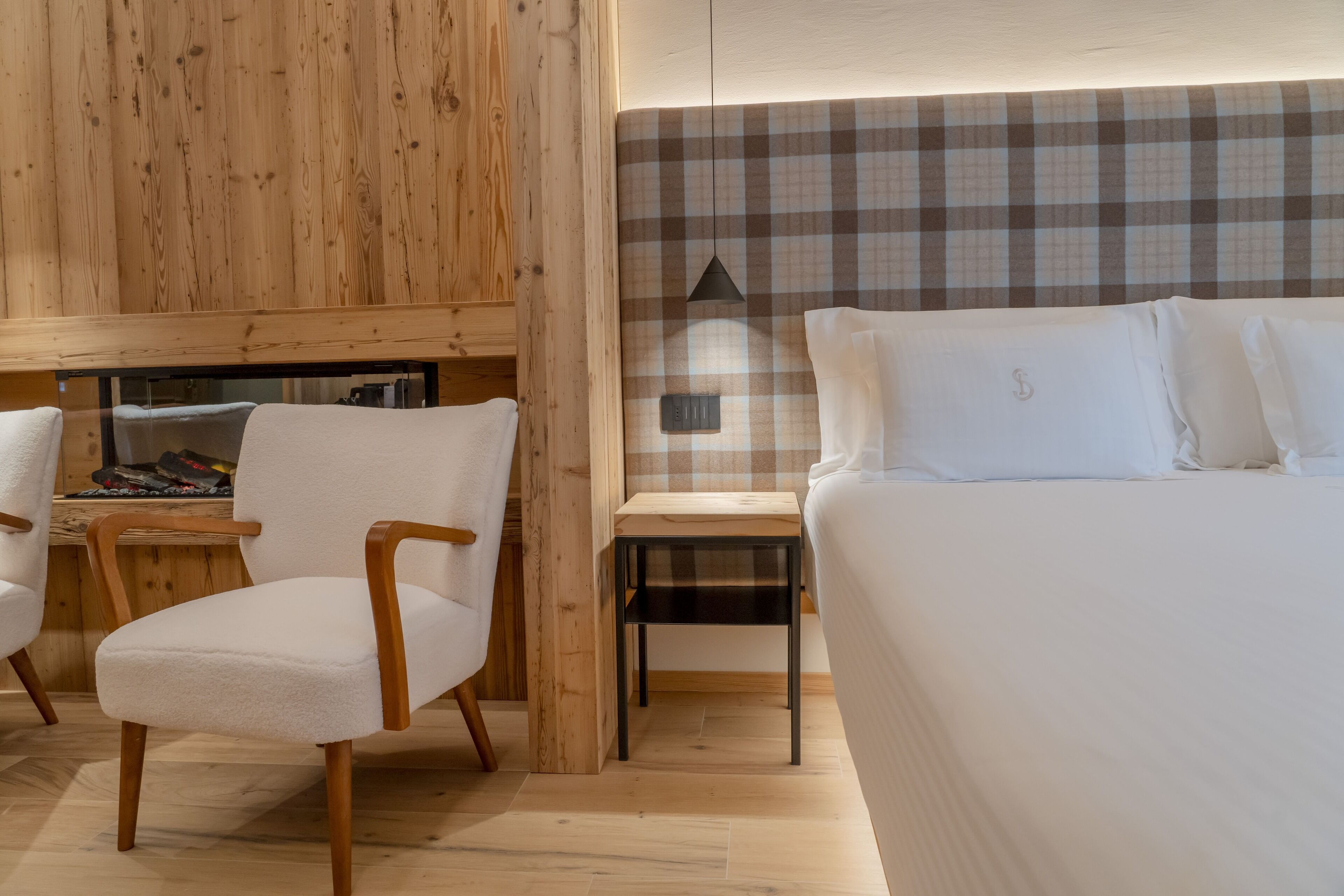 Habitació d'hotel moderna amb paret de fusta, capçalera amb quadres, llit amb roba blanca, taula de fusta petita i una cadira.