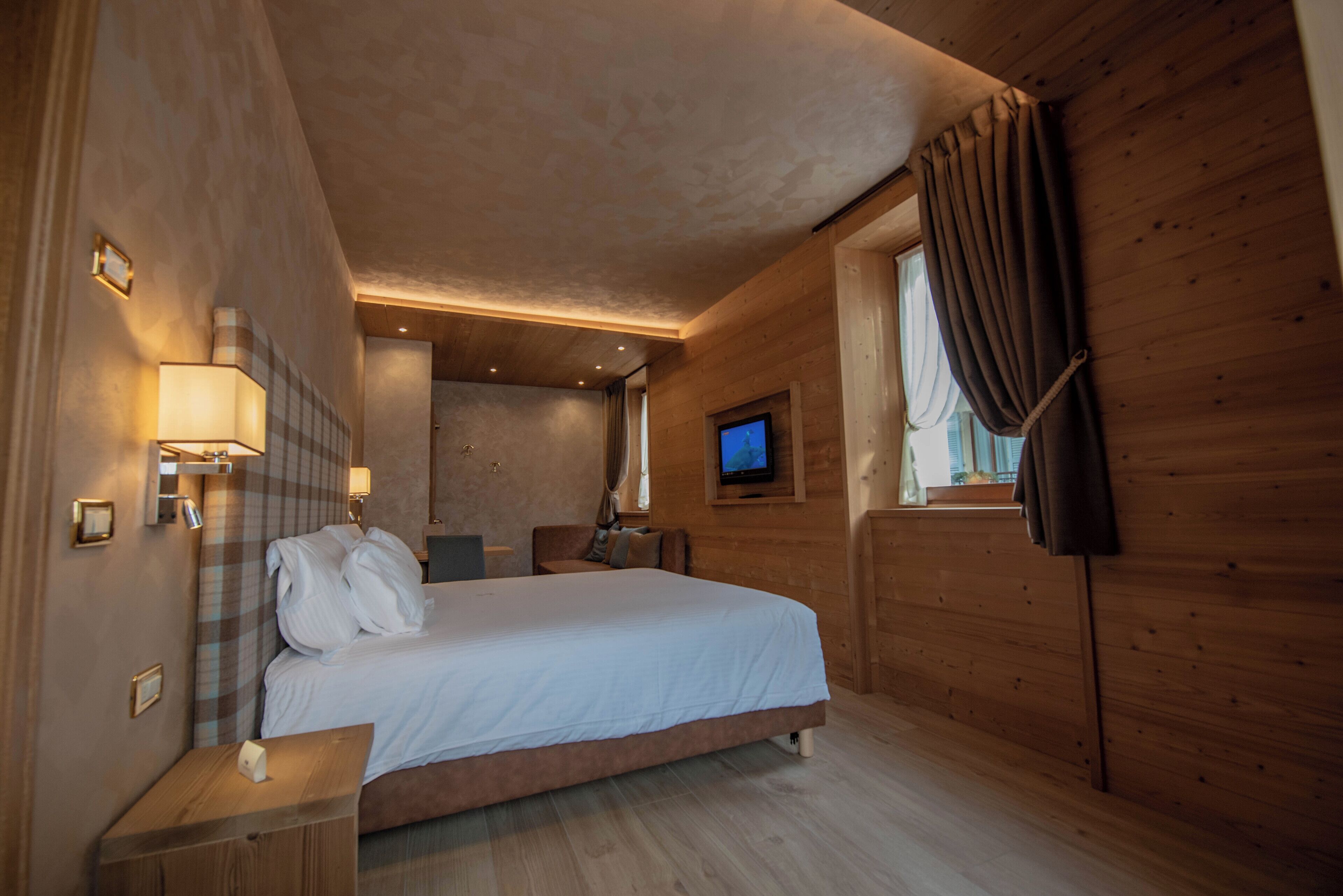 Ein Hotelzimmer mit einem großen Bett, einem an der Wand befestigten Fernseher und Holzvertäfelung.
