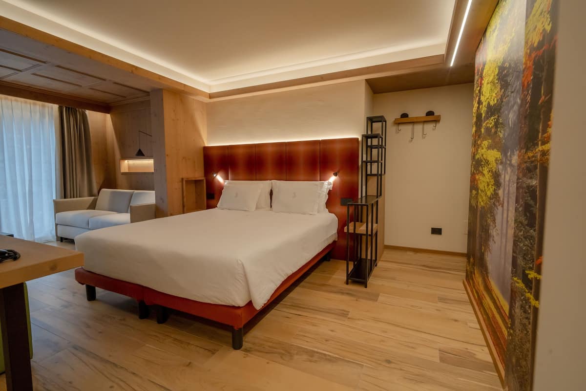A hotel room with a large bed, a desk, a chair, a nightstand, and a painting on the wall.