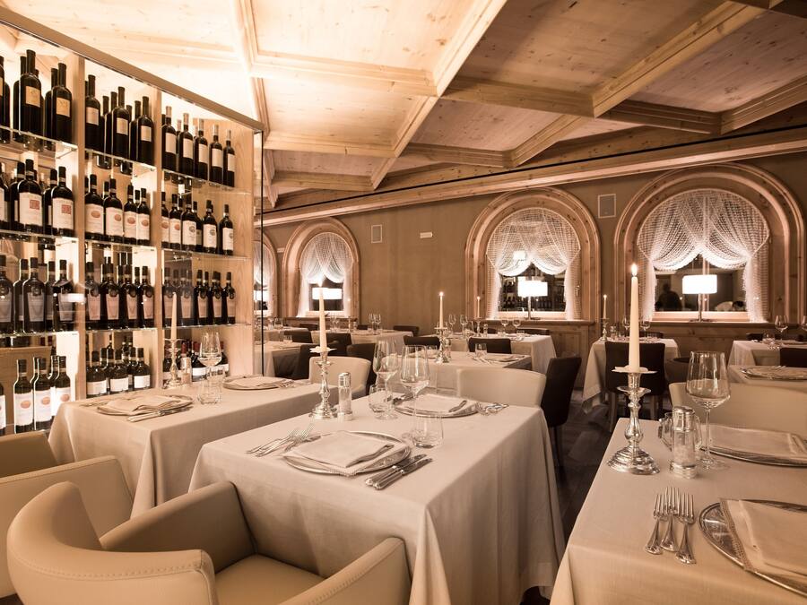 A restaurant with multiple tables set for dining, a wine rack with various bottles, and arched windows with decorative lighting.