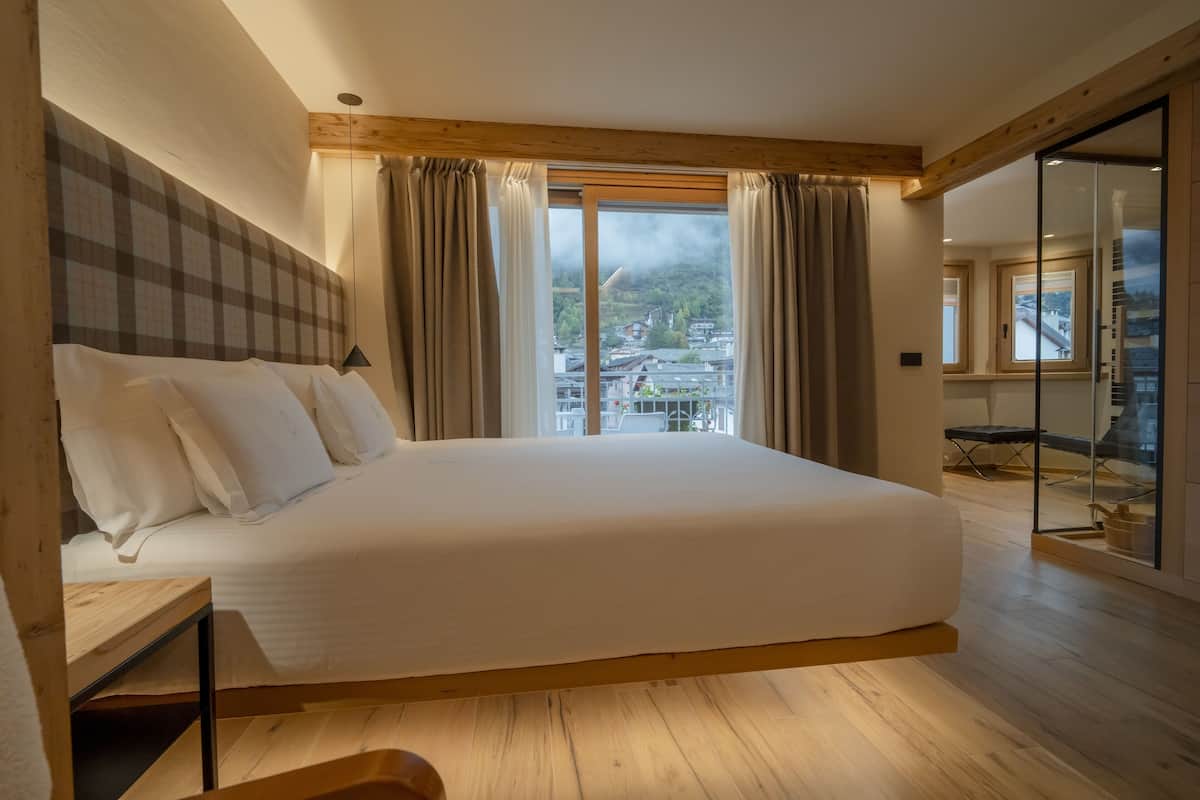 A bedroom with a large bed, wooden floor, and a view of a town through a window.