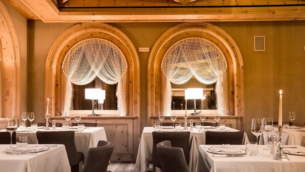 A restaurant with multiple tables set for dining, featuring arched windows with decorative drapes and warm lighting. - San Lorenzo (Bormio)