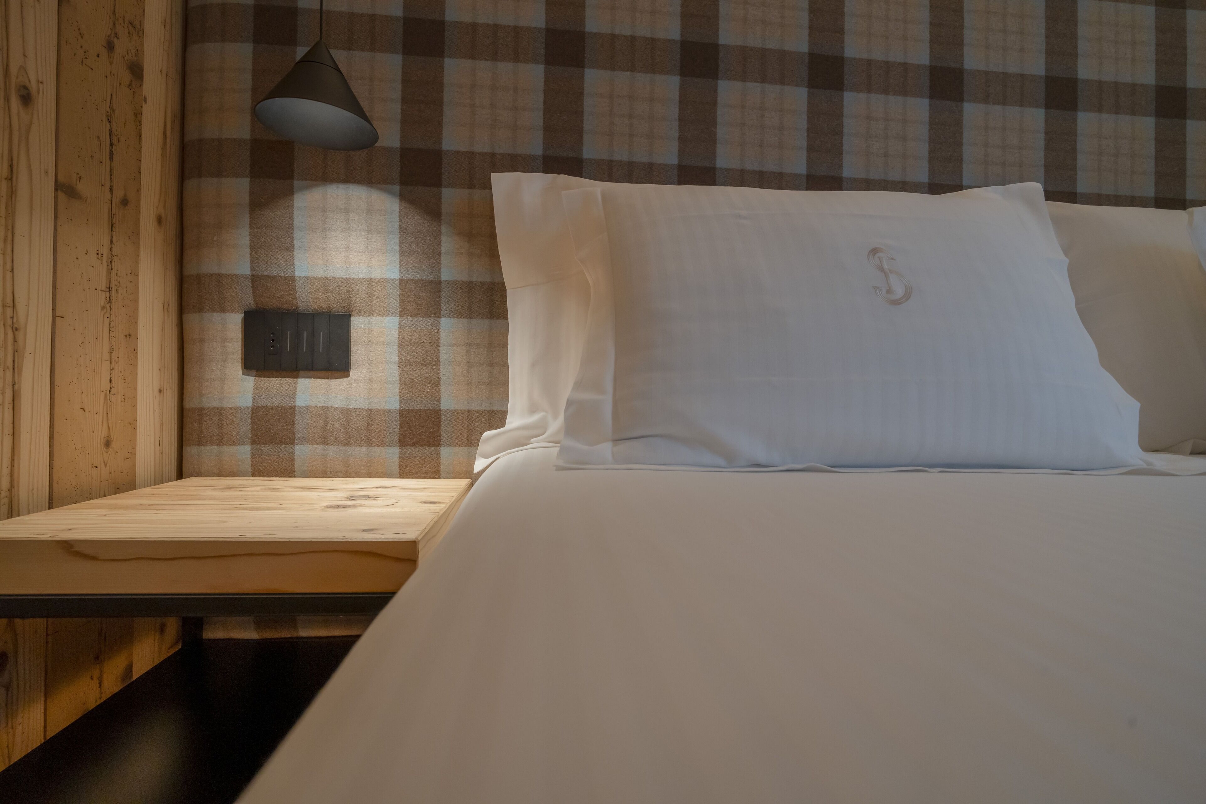 A wooden bed with white bedding and a checkered wall pattern.
