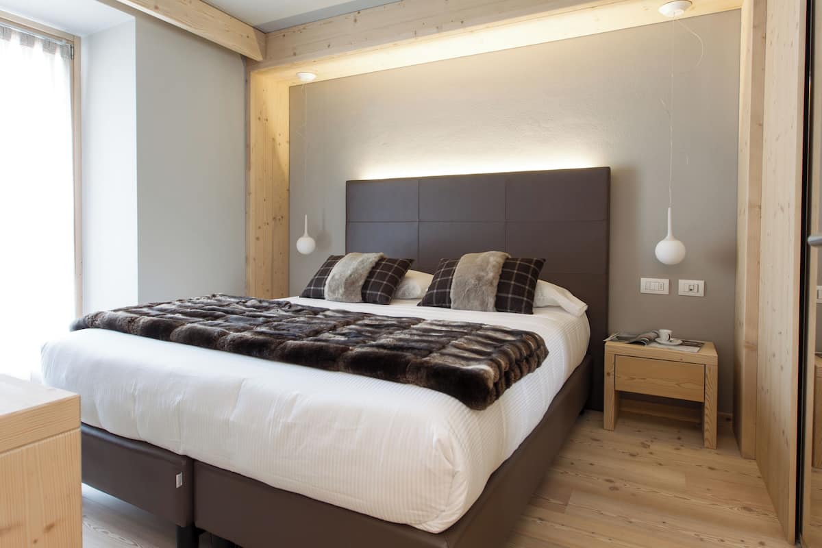 A modern bedroom with a large bed, wooden headboard, bedside tables, and a hanging light fixture.