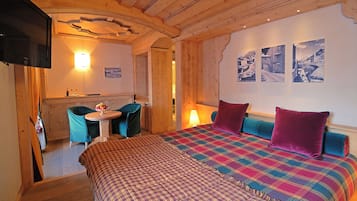 Ein gemütliches Zimmer mit Bett, einem kleinen Tisch mit Obst, einem Fernseher und einer Wand mit Bildern.
