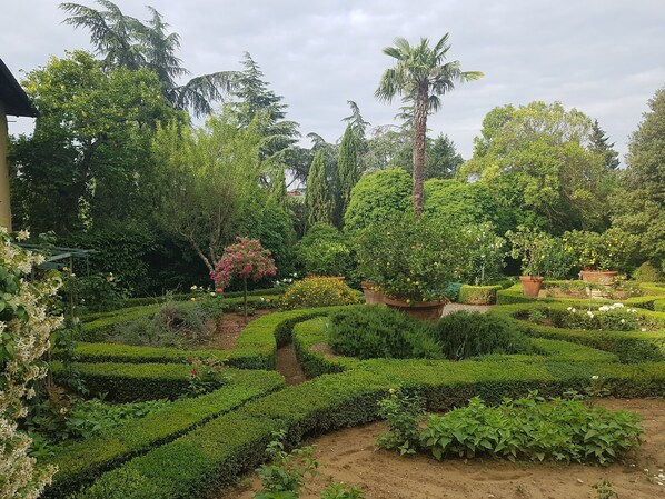 Un jardín bien cuidado con setos ordenados, diversos árboles y plantas con flores.