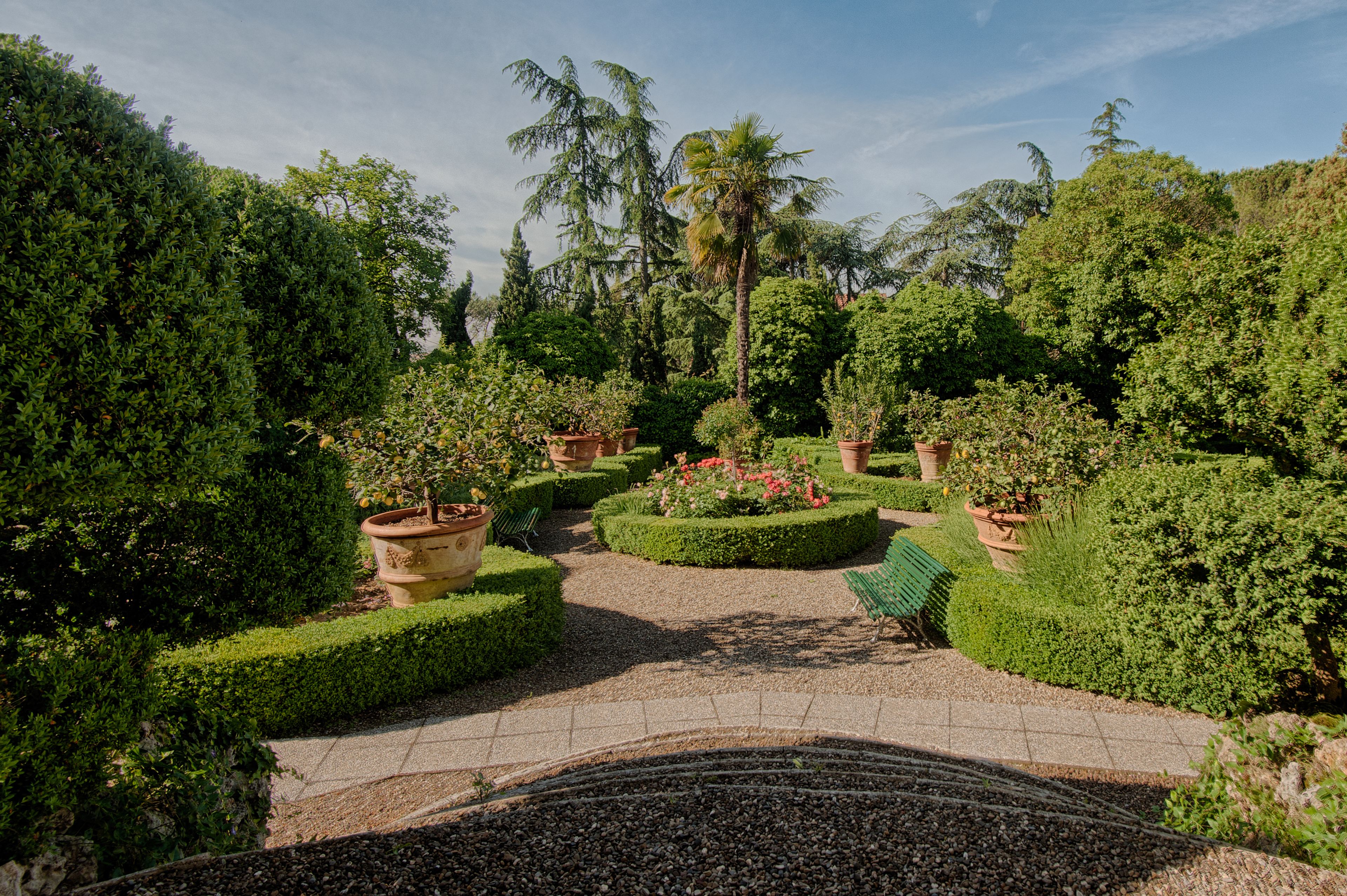 A formal garden with neatly trimmed hedges, potted plants, and a gravel pathway.