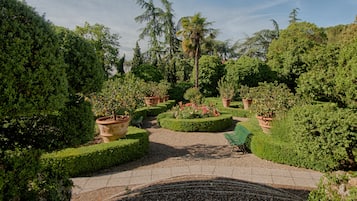 A formal garden with neatly trimmed hedges, potted plants, and a gravel pathway.