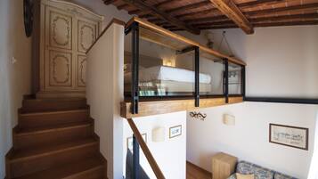 Una escalera con escalones de madera que lleva a un dormitorio entrecubierto con una cama y un ventanal.
