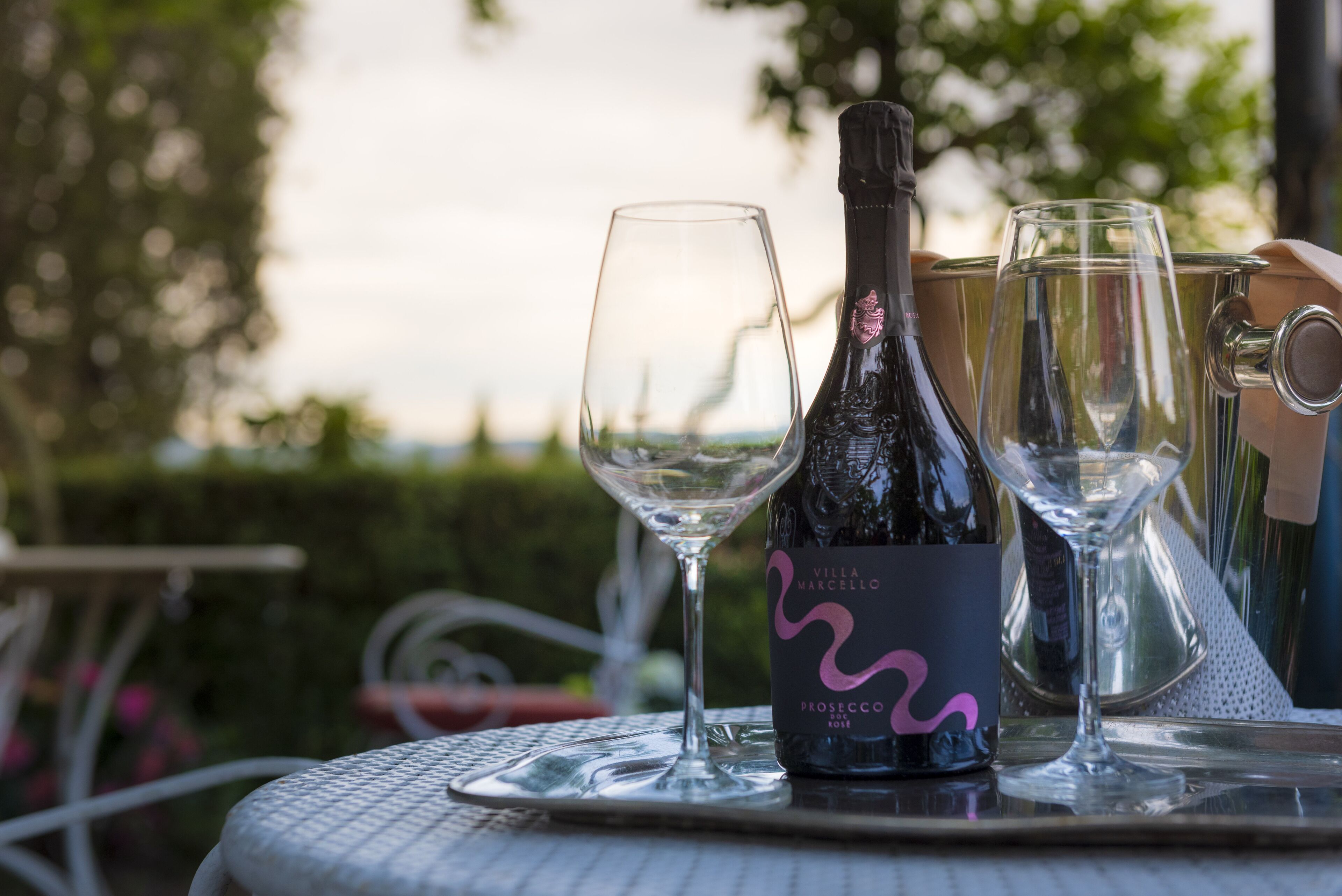A bottle of wine and two glasses on a table outdoors.