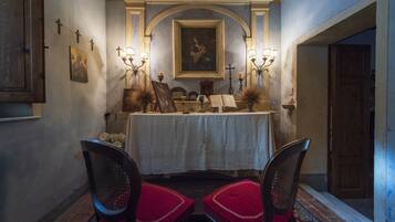 A chapel with a white altar, religious paintings, and candles. There are two chairs in front of the altar.
