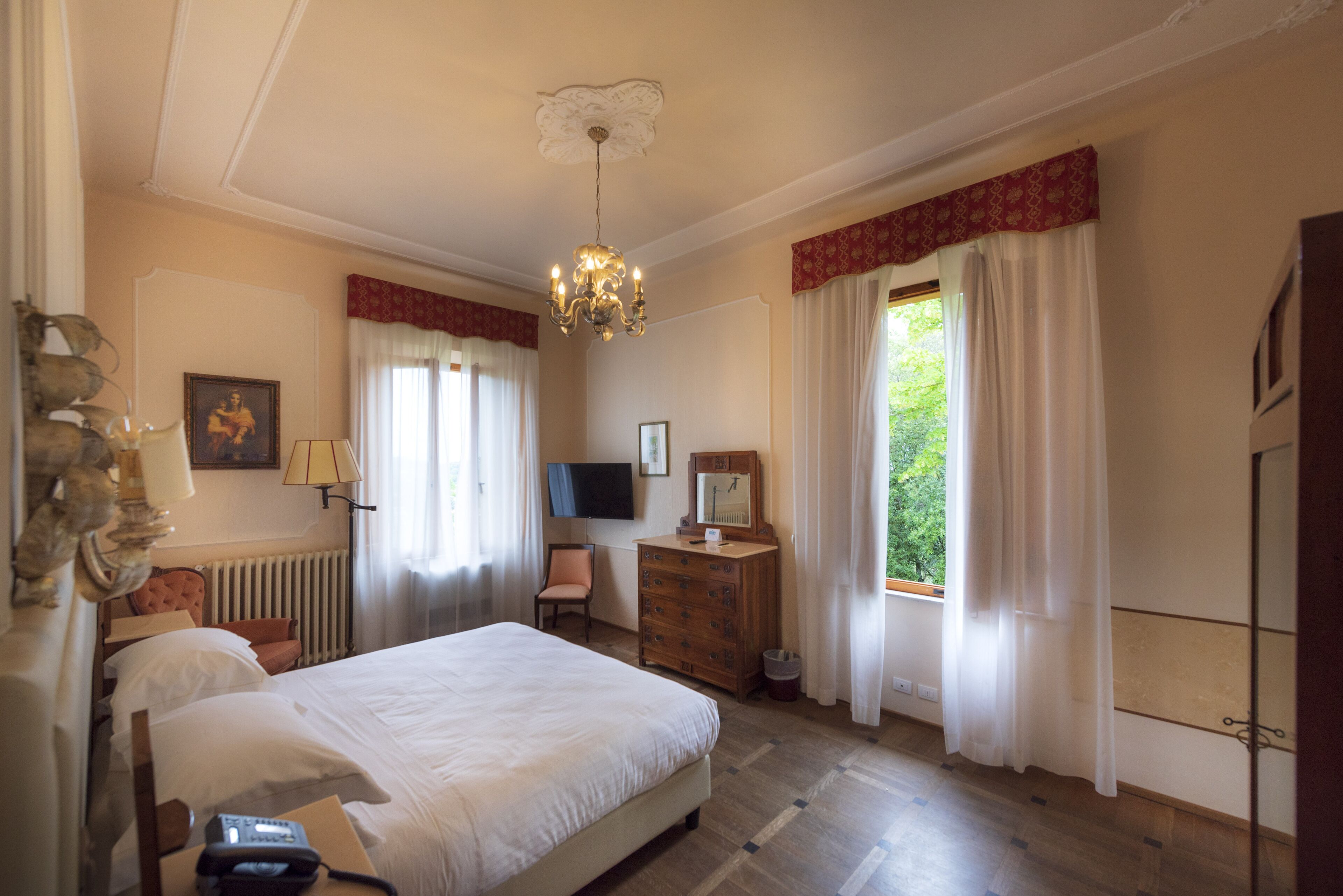 Une chambre d’hôtel avec un grand lit, une commode en bois, un bureau avec une chaise, une télévision et une fenêtre avec des rideaux.
