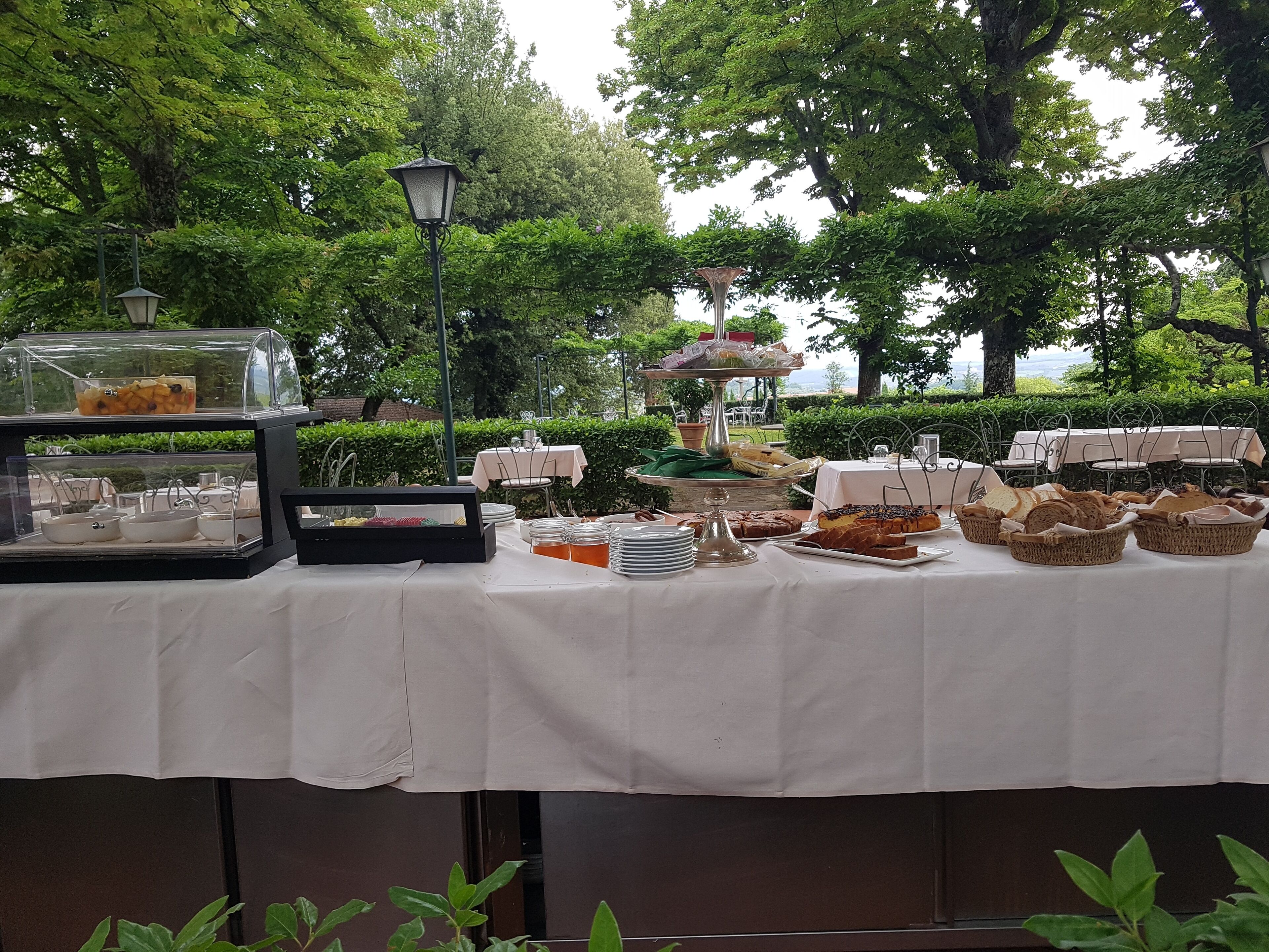 Ein Buffet mit verschiedenen Speisen und einer Glastheke, draußen gelegen, mit Bäumen und einer Lampe im Hintergrund.