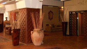 A lobby with a central seating area, a large vase with tall plants, and a patterned rug. - Grand Hotel Boston (Chianciano Terme)