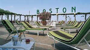 A rooftop lounge area with green-striped lounge chairs and a sign that reads "BOSTON". - Grand Hotel Boston (Chianciano Terme)