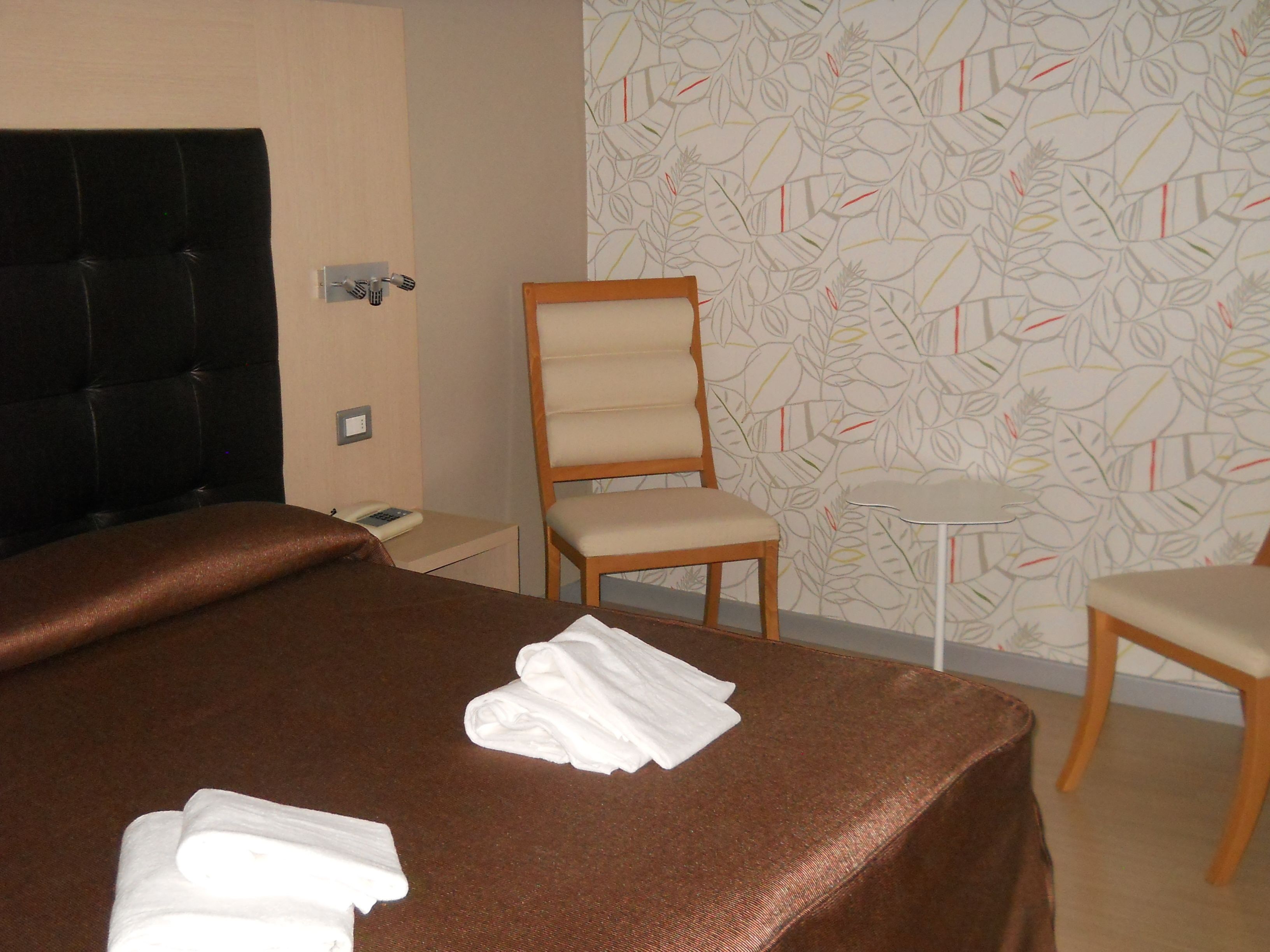 Una camera d'albergo con un letto grande, una sedia di legno, un tavolino e una carta da parati decorata.