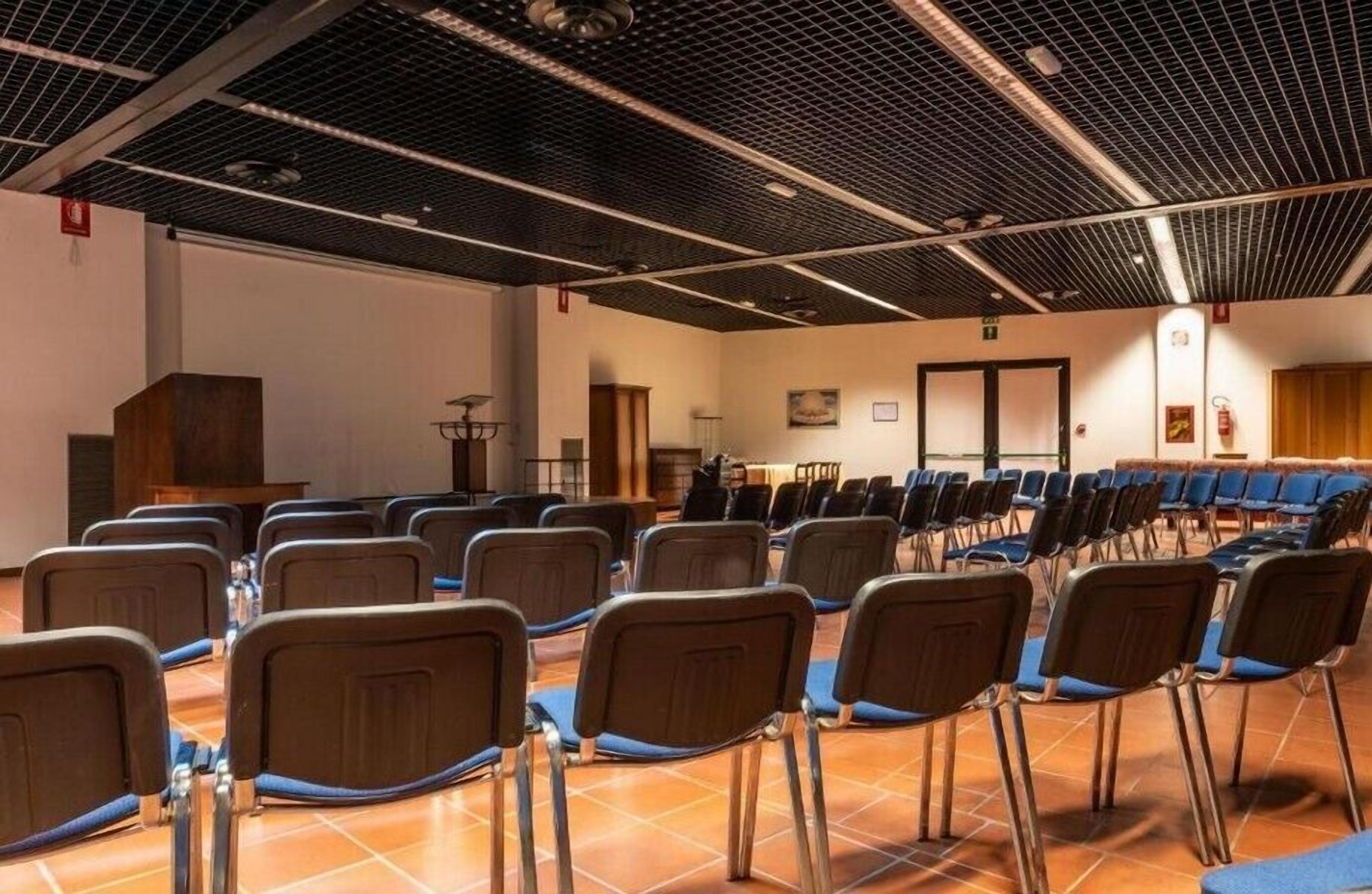 Une salle de conférence avec des rangées de chaises, un pupitre et un sol carrelé.