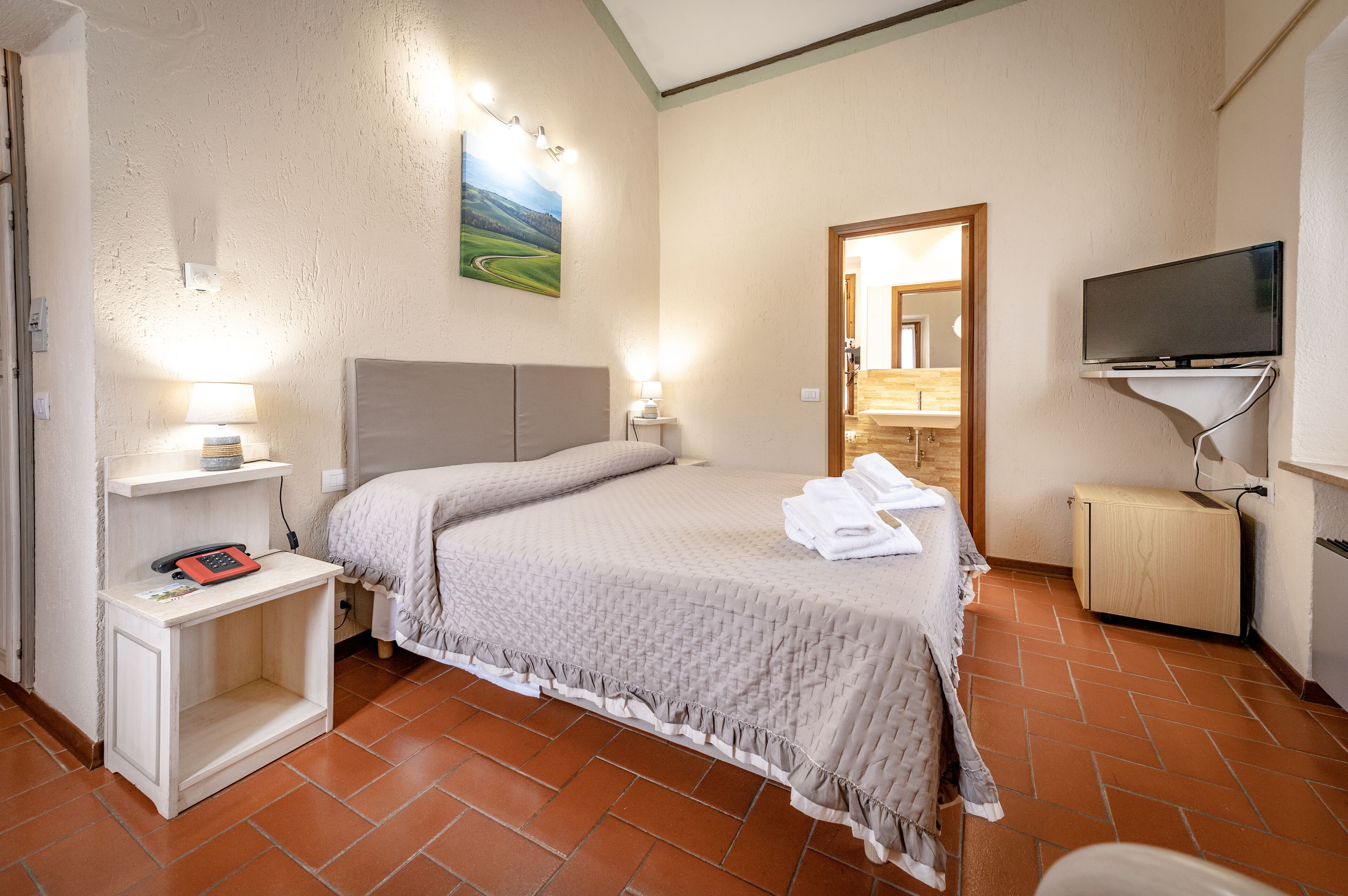 Un dormitorio con cama, lámparas de noche, un televisor de pantalla plana, un mueble bajo y un cuadro en la pared.