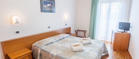 A neatly arranged bedroom with a wooden bed, bedside tables, a small desk, a television, and a framed picture on the wall.