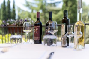 Una mesa con botellas de vino y copas, colocada al aire libre con un jardín desenfocado de fondo.
