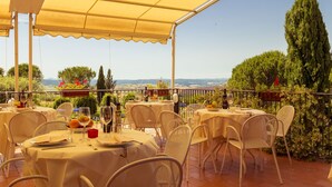 An outdoor dining area with tables and chairs, covered by a canopy, overlooking a scenic landscape. - Palazzuolo (San Quirico d'Orcia)