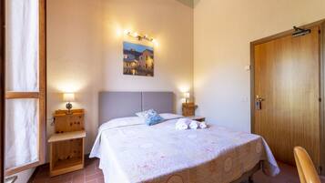 Un dormitorio con cama, lámparas de noche, una mesita de noche de madera, una puerta y un cuadro en la pared.