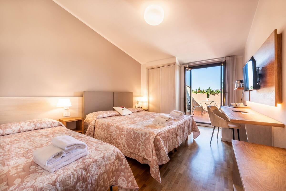 Habitación de hotel con dos camas, un escritorio y vistas al exterior.