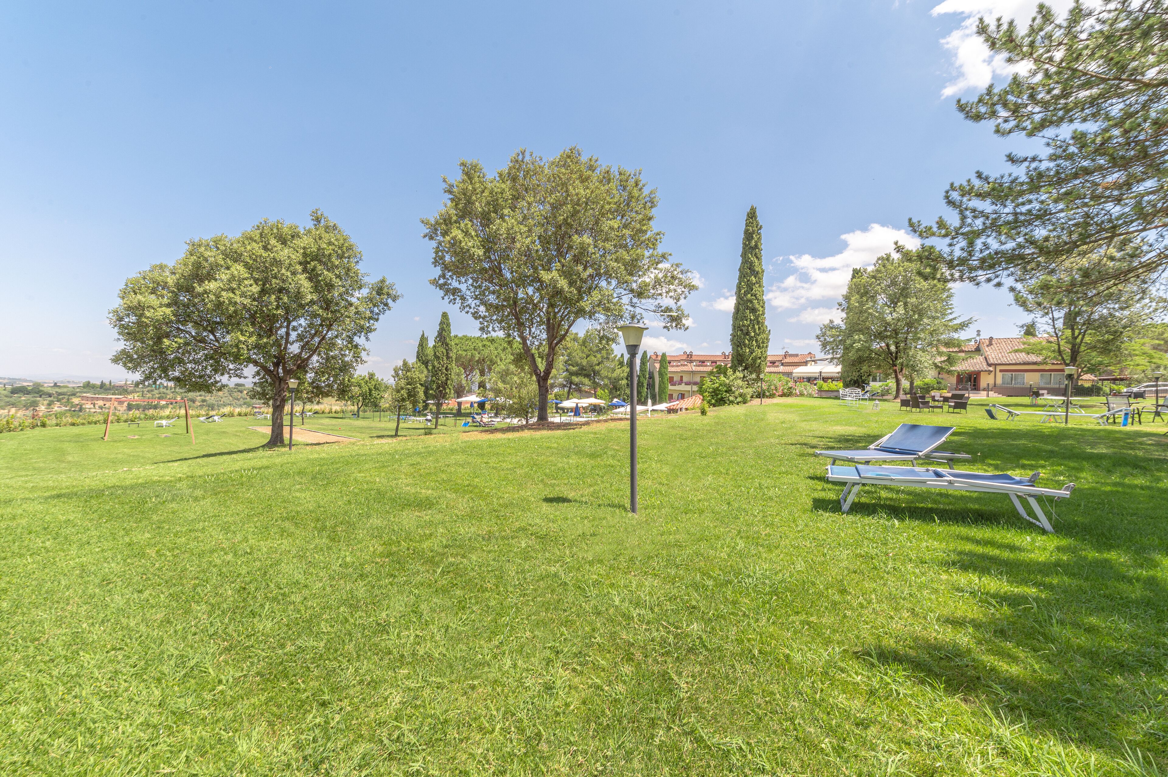 A grassy area with two sun loungers, a lamp post, and a tall tree.