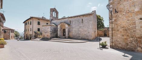 A historic stone building with a central archway, a bell tower, and a paved courtyard.