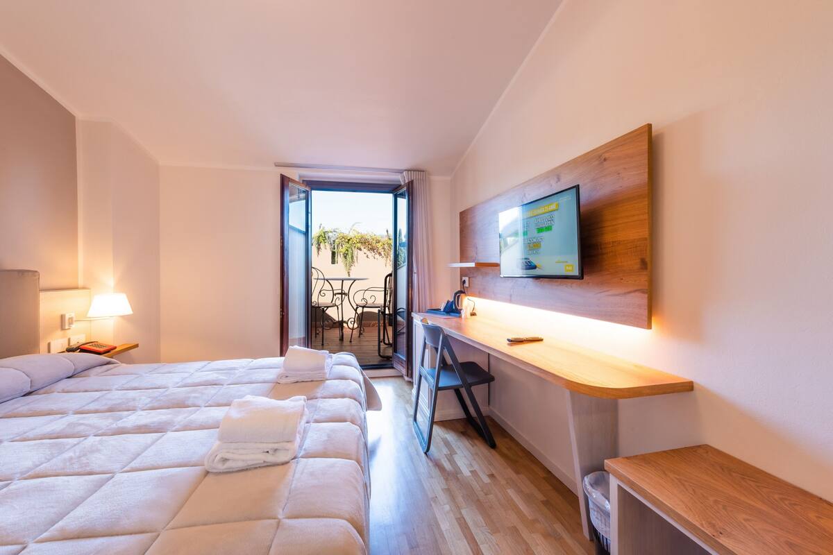 Habitación de hotel con cama, escritorio, televisor y vistas al exterior.