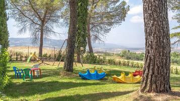 Explore a serene outdoor play area with swings and boats amidst a lush grassy field and surrounding trees.