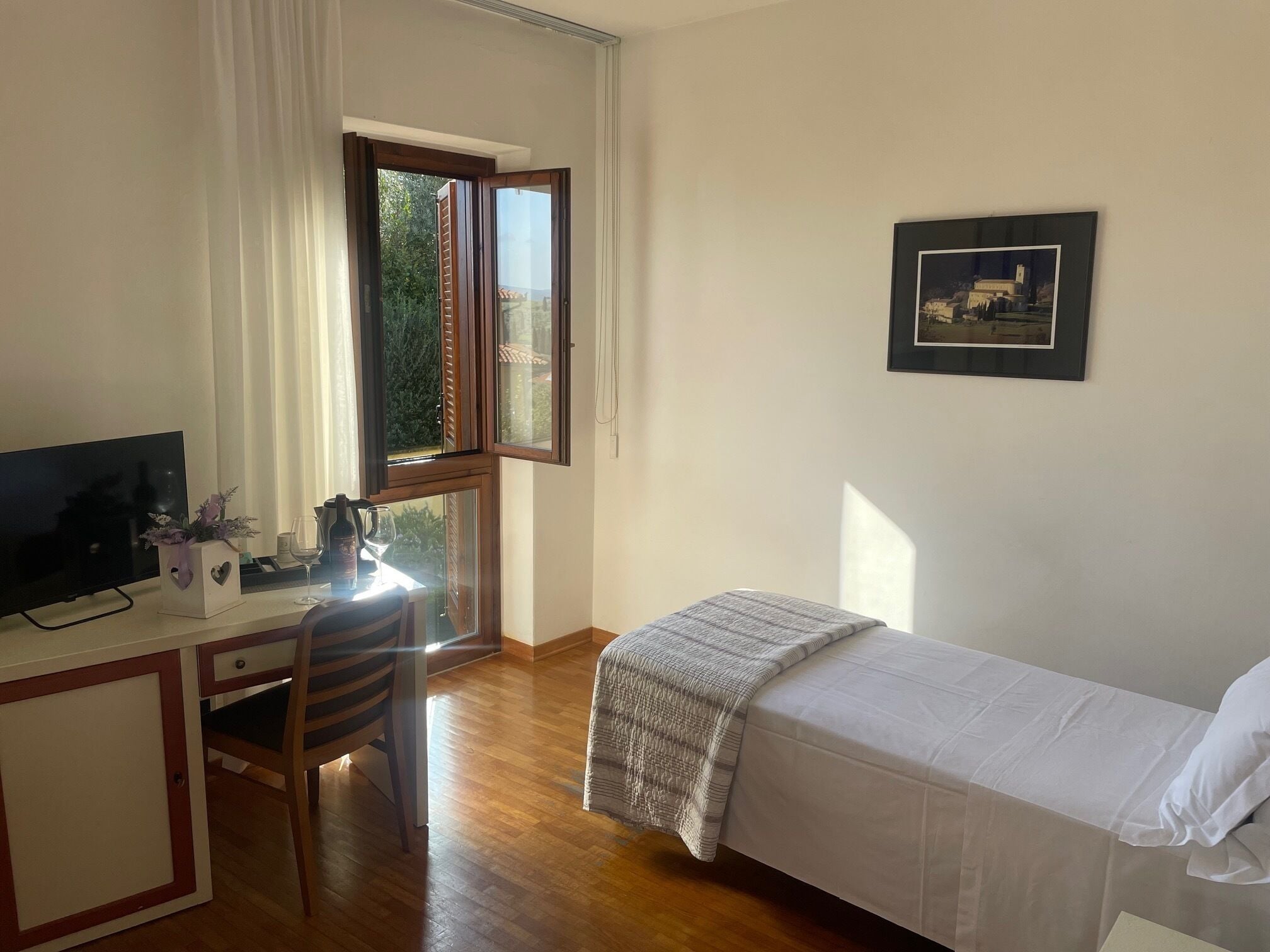 Ein Schlafzimmer mit Bett, Schreibtisch inklusive Computer, Stuhl und einem Fenster mit Vorhängen.