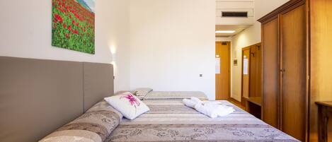 A hotel room with a large bed, a painting on the wall, and a wooden wardrobe.
