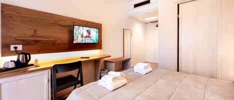 A hotel room with a bed, a desk with a kettle, a chair, a TV, and a wardrobe.