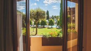 A view through a window of a courtyard with a pool, trees, and a building in the background. - Palazzuolo (San Quirico d'Orcia)