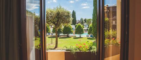 A view through a window of a courtyard with a pool, trees, and a building in the background.