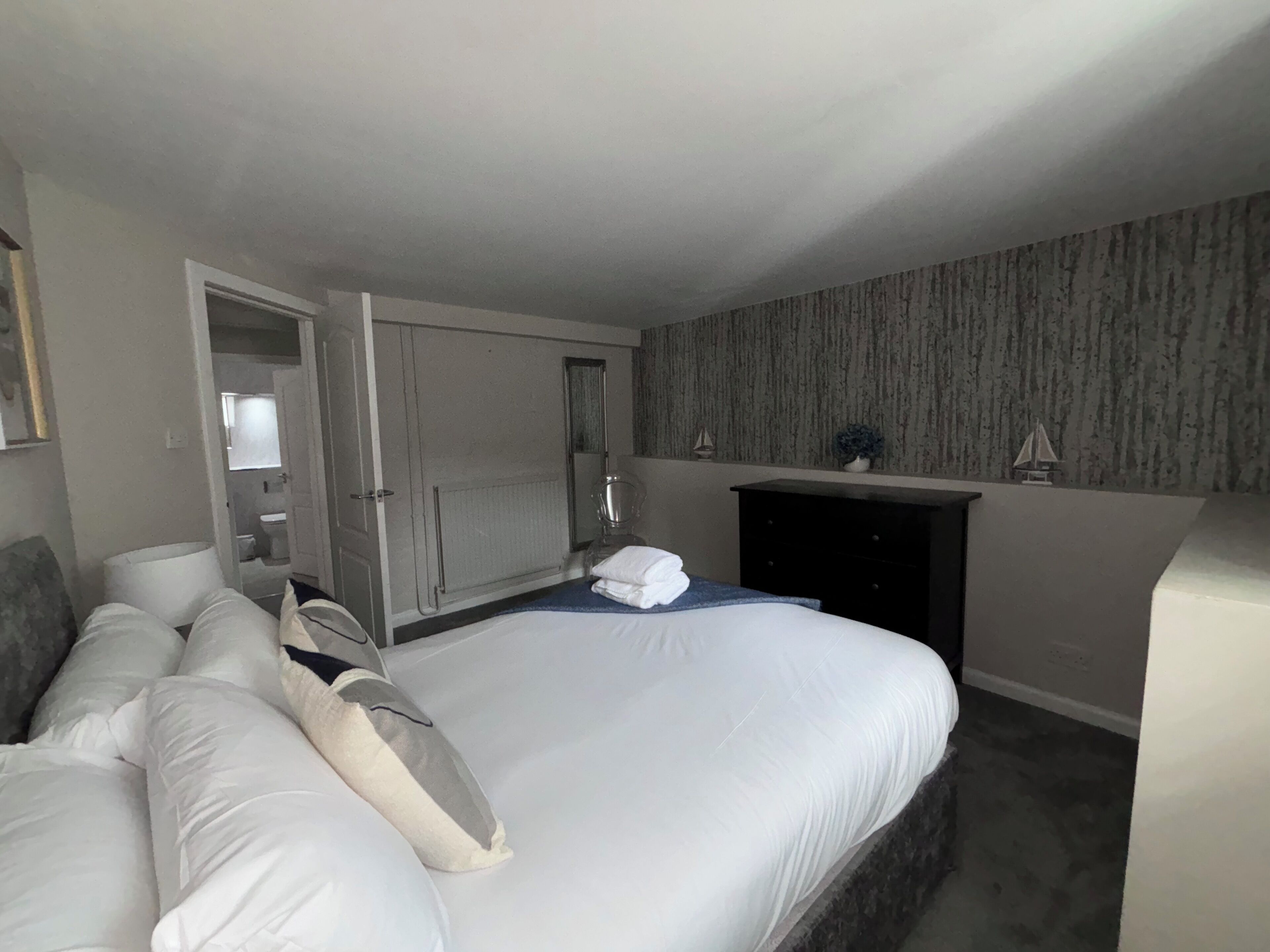 A bedroom with a large bed, a dresser, a mirror, and a fireplace.