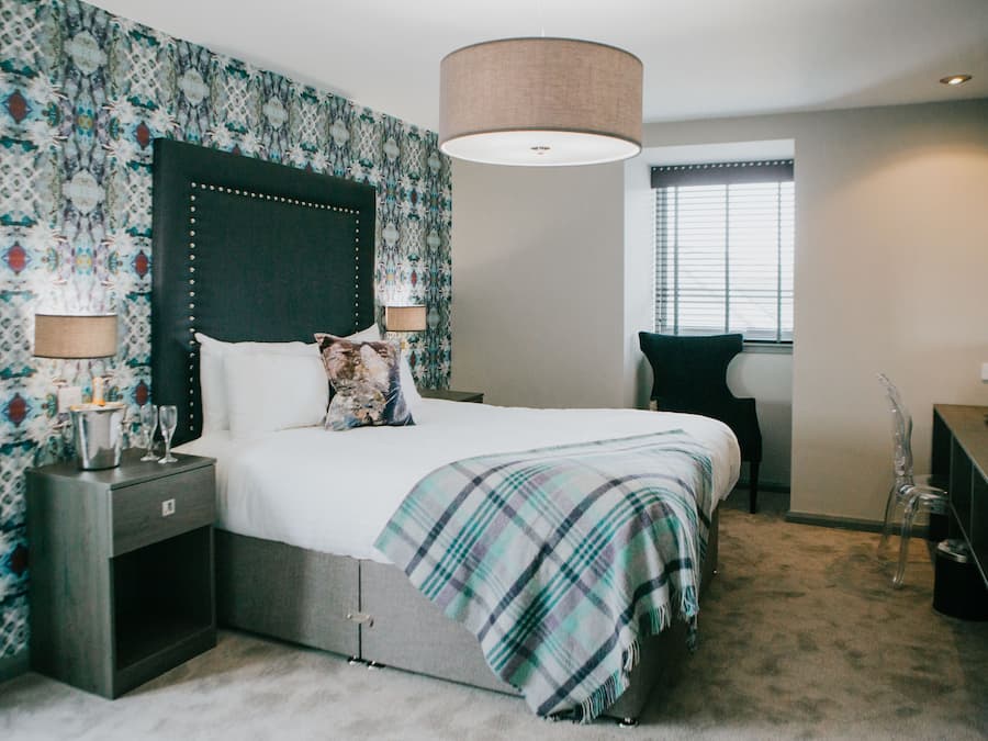 Une chambre avec un grand lit, deux tables de chevet, une commode, une chaise, un bureau et une fenêtre avec des stores.