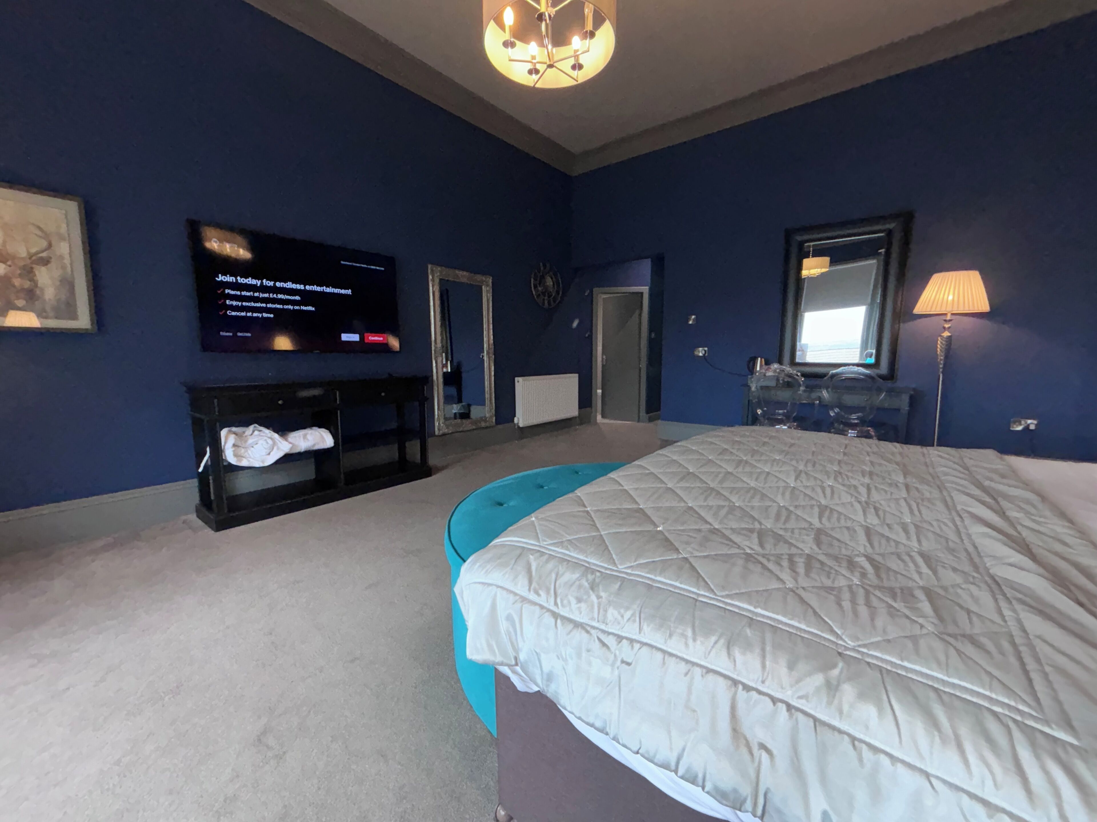 Un dormitorio con una cama grande, un televisor en la pared, un aparador y un espejo.
