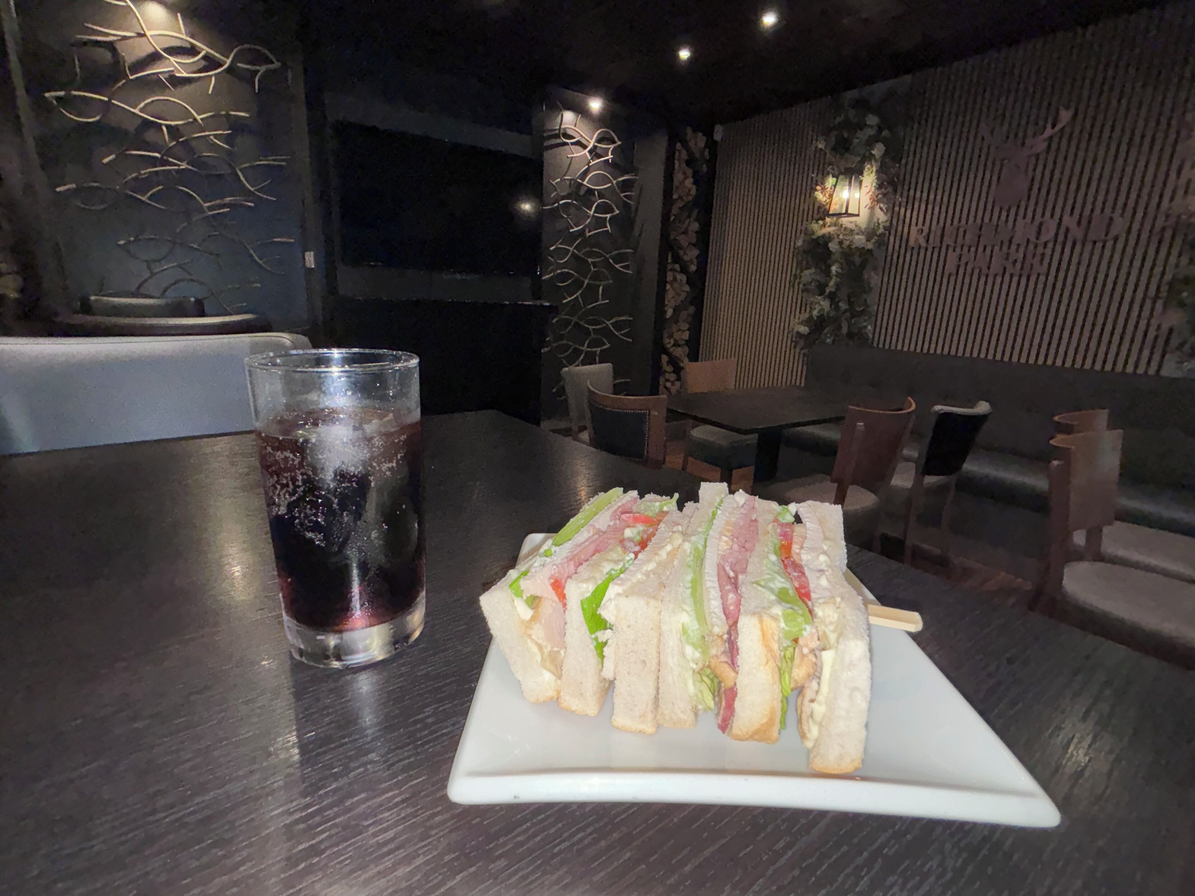 A table with a sandwich and a glass of soda in a dimly lit restaurant.