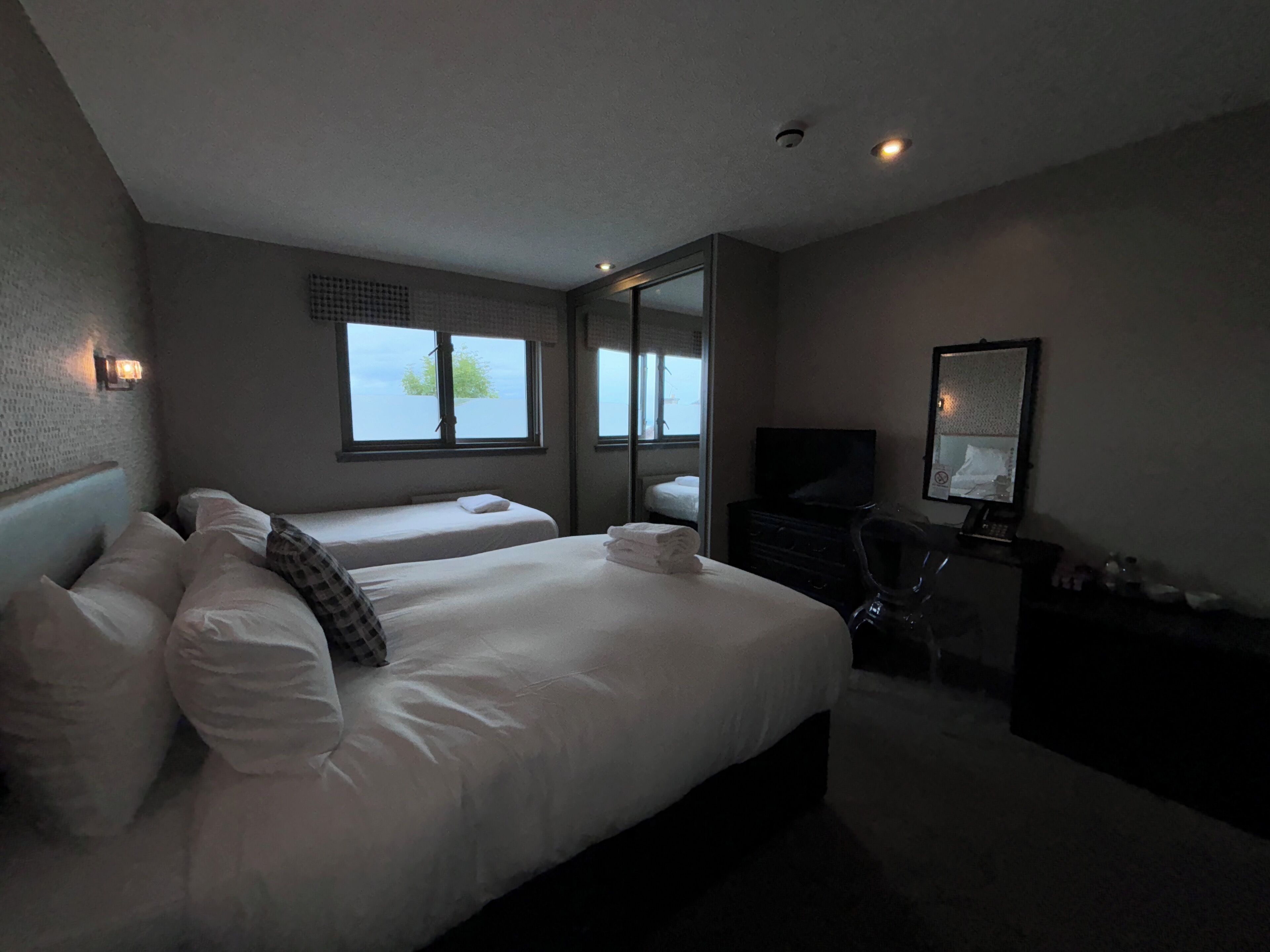 A hotel room with two beds, a dresser, a TV, and a large window.