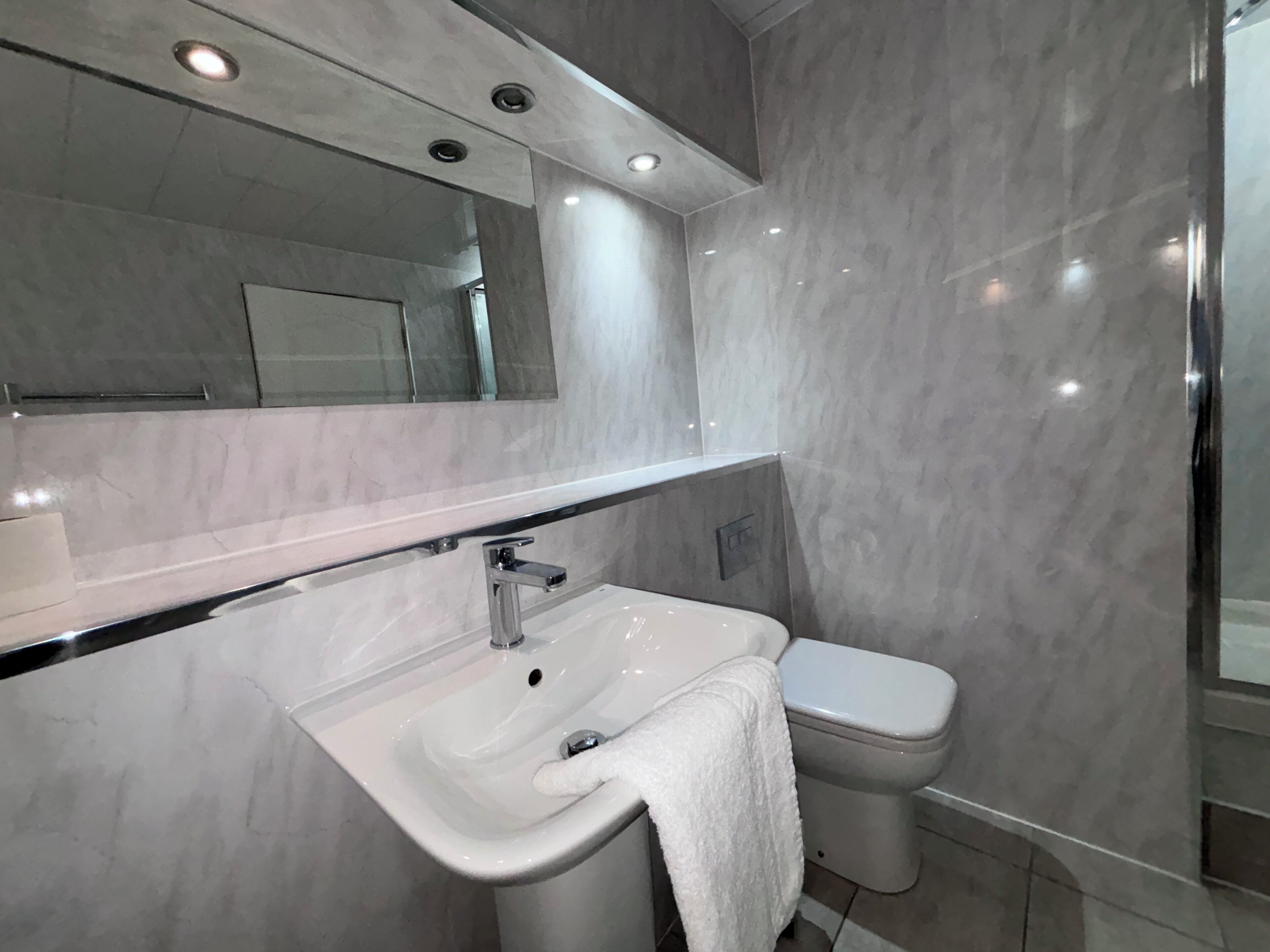 Une salle de bain moderne avec un lavabo blanc, des toilettes et un miroir au-dessus du lavabo.