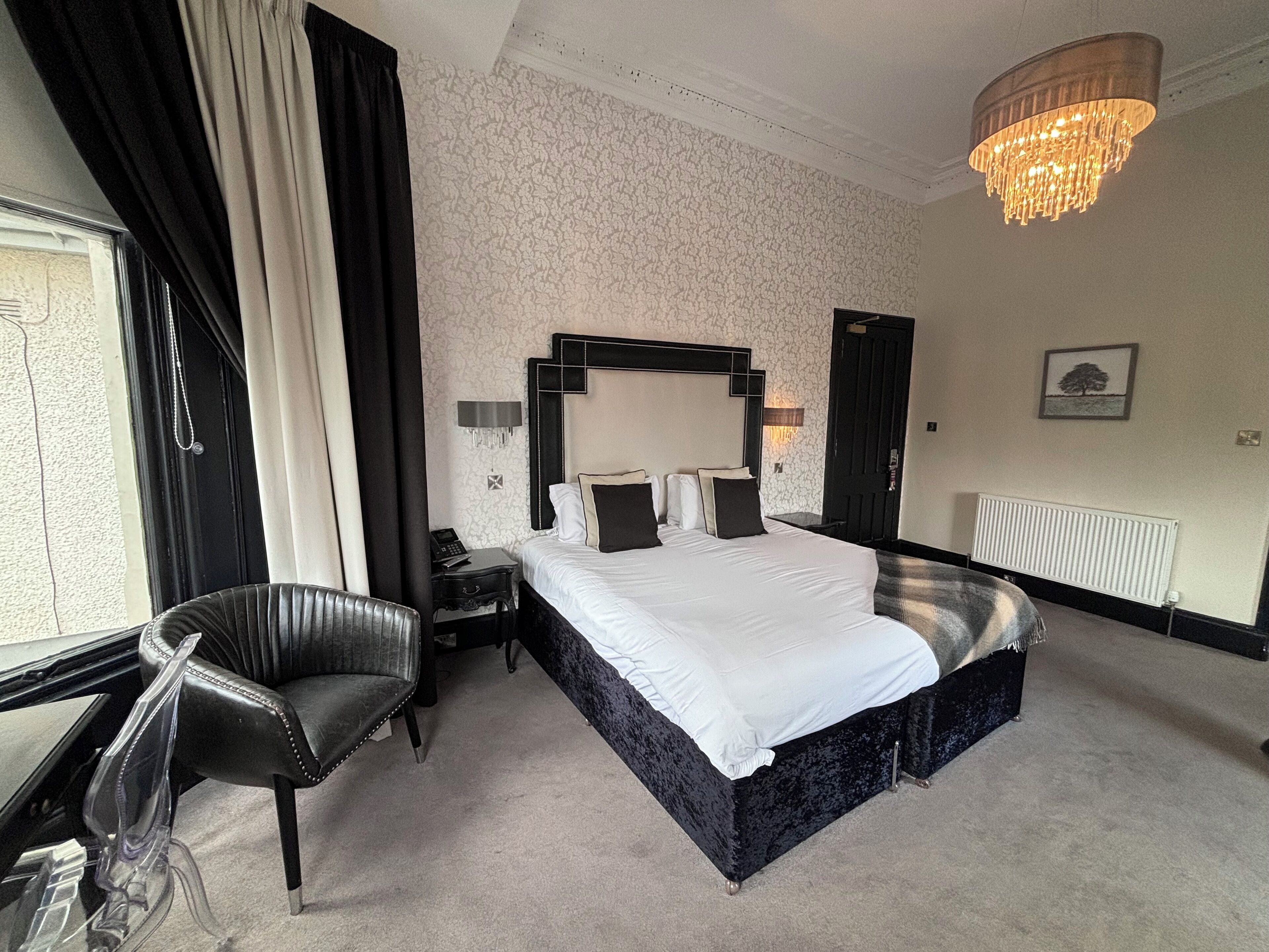 Une chambre d’hôtel avec un grand lit, un bureau, une chaise et un lustre.