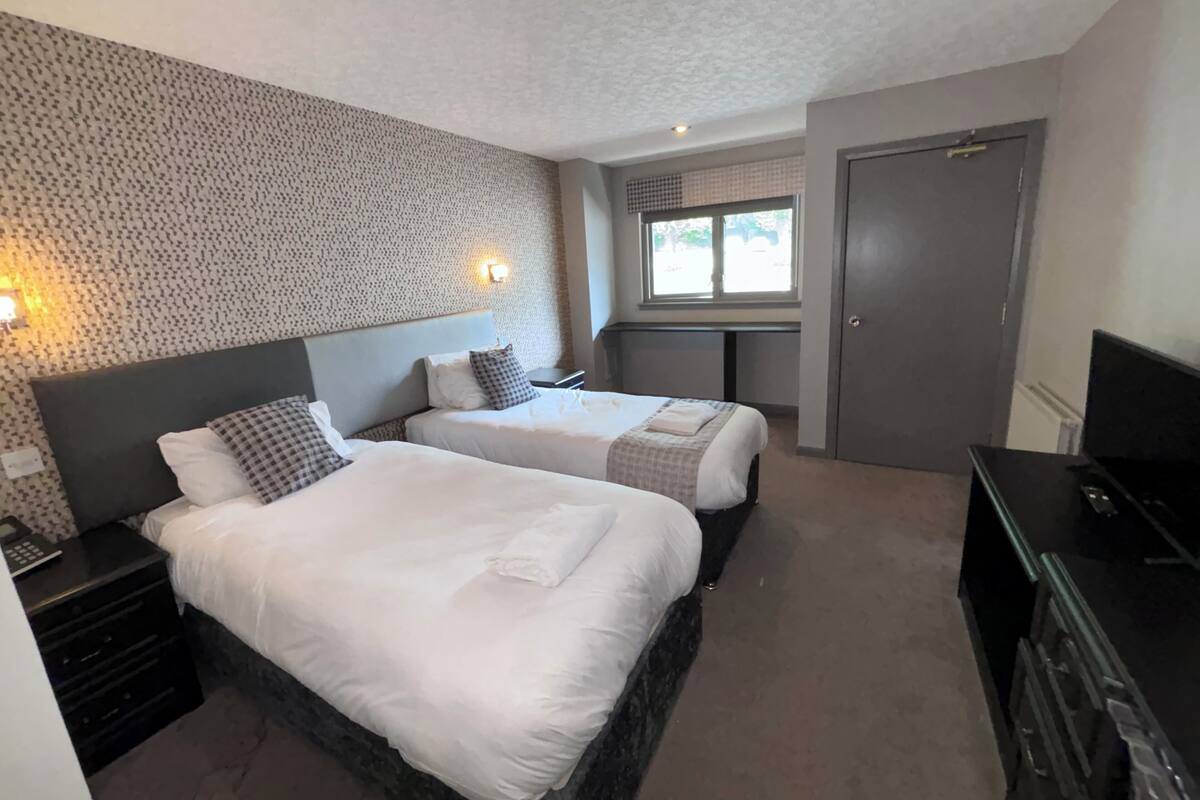 Ein Hotelzimmer mit zwei Betten, einem Schreibtisch, einem Fernseher und einem Fenster.