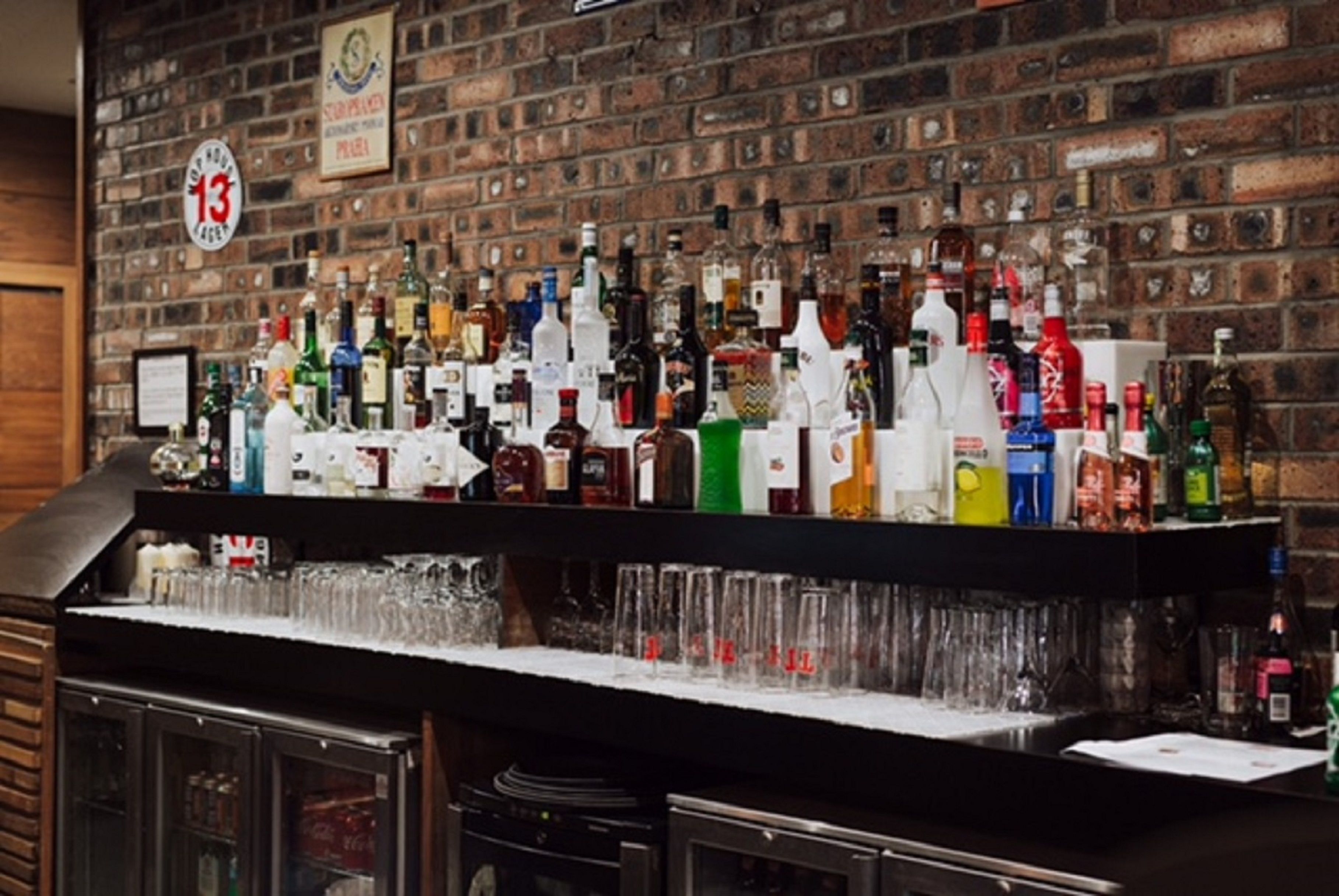 Zona de bar con pared de ladrillo, estantes llenos de botellas y vasos de distintos tipos.