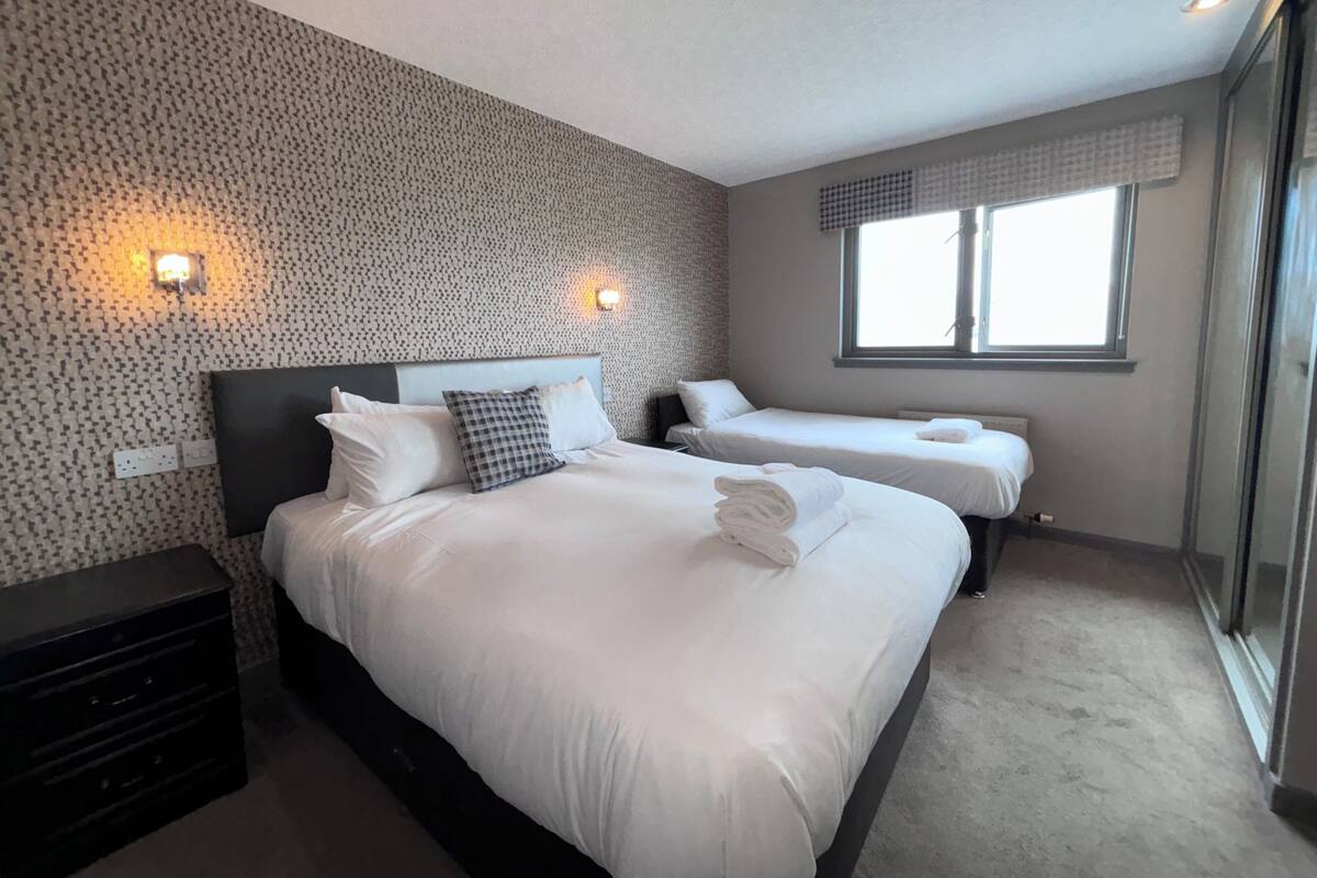 Ein Hotelzimmer mit zwei Betten, einer Wand mit Muster und einem Fenster mit Vorhängen.