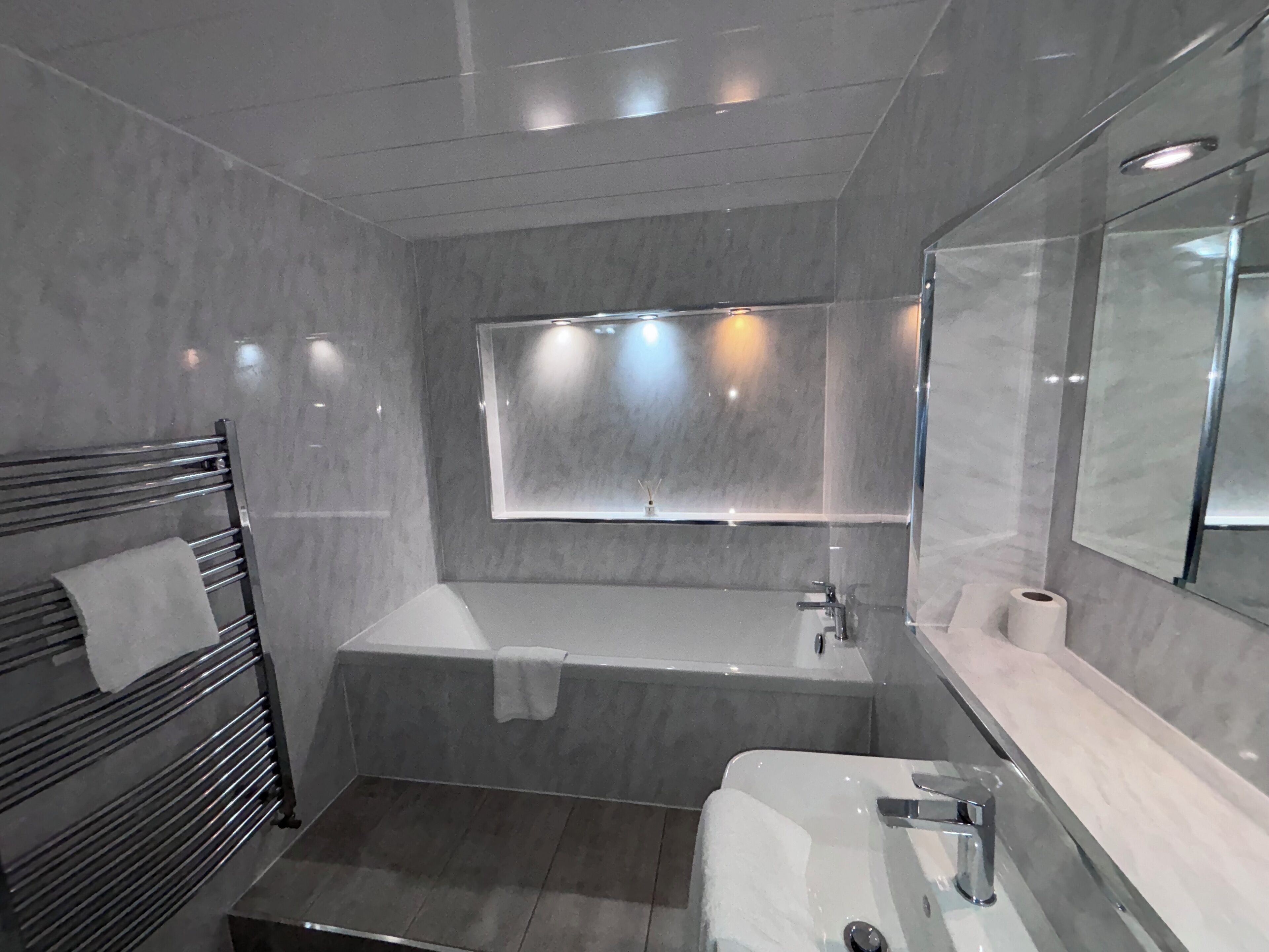 Un baño moderno con ducha envuelta en vidrio, un espejo grande y un perchero para toallas.