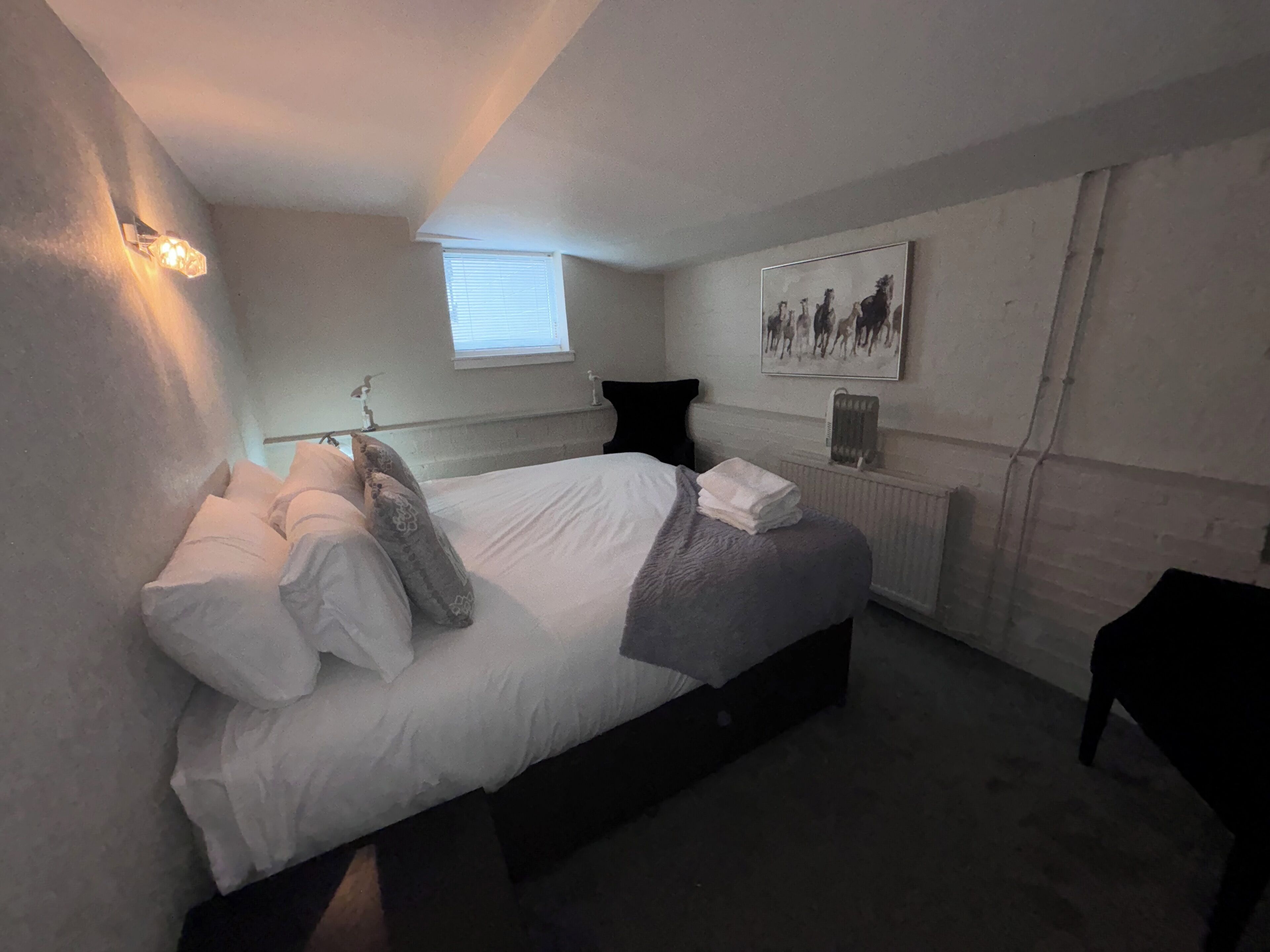 A bedroom with a bed, pillows, a radiator, a window, and a wall-mounted picture.