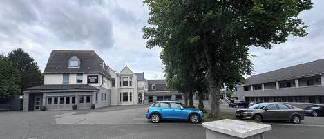 A hotel with a restaurant, a blue car parked in front, and a tree.